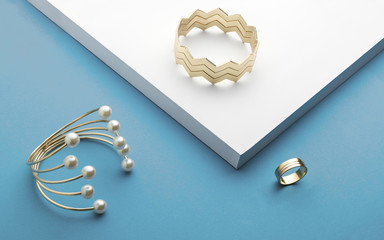 Golden bracelets and golden ring on white and blue background - Zigzag bracelet and pearl golden bracelet
