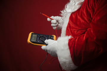 Closeup on Santa Claus solving electricity problems using holding digital tester multimeter electronic measure equipment. Ready for Merry Christmas and Happy New Year celebration background.