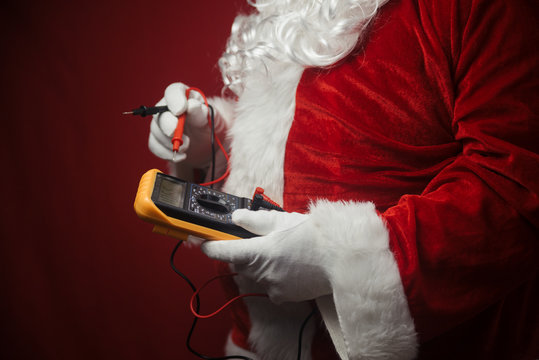 Closeup on Santa Claus solving electricity problems using holding digital tester multimeter electronic measure equipment. Ready for Merry Christmas and Happy New Year celebration background.