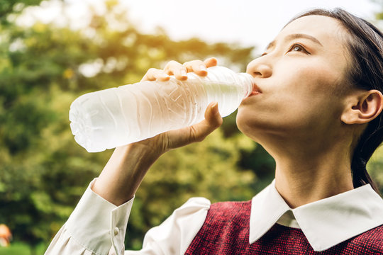 Beautiful asia woman drinking water from a bottle while relaxing  and feeling fresh on green natural background at summer green park. Healthy lifestyle concept