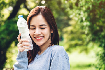Beautiful asia woman holding water bottle while relaxing and feeling fresh on green natural background at summer green park. Healthy lifestyle concept