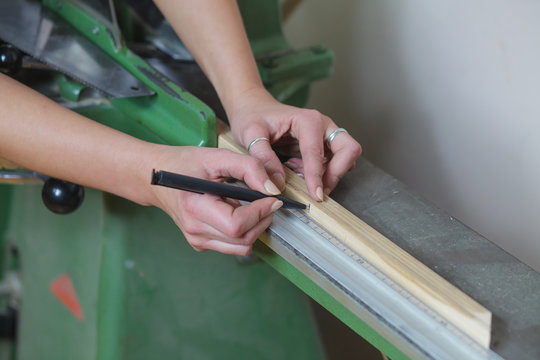 woman worker measuring and marking picture frame wood plank before cutting