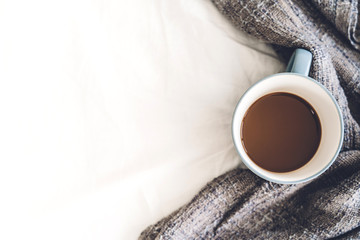 Cup of hot coffee and warm scarf on white bed.Winter and cold weather concept