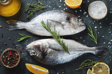 Two fresh raw Dorado fish with spices and olive oil on a dark stone table. Top view. Flat lay