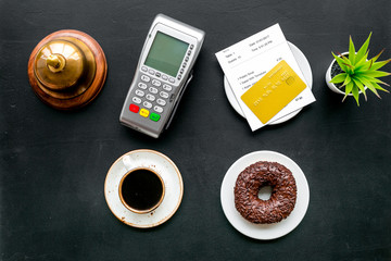 Payment terminal on restaurant desk near bill, service bell, coffee on black background top view