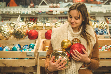 Fototapeta na wymiar Girl in a warm coat holding large ball for Christmas tree in a mall at the Christmas Fair
