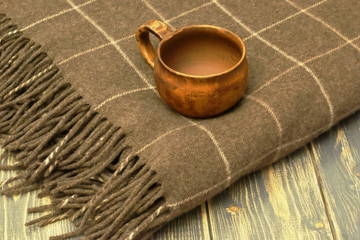 Fototapeta na wymiar Antique old clay cup and warm, soft woolen plaid on dark natural wooden background.