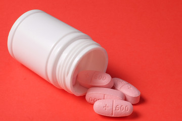 White pills and bottle on red background