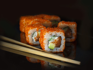 Japanese rolls and sticks are served on a black background with reflection.