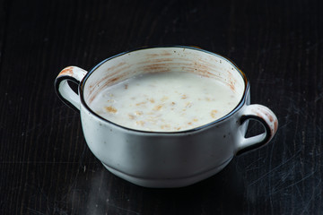 Morning Breakfast, oatmeal on milk with butter in white plate on dark background