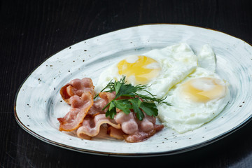 Scrambled eggs and bacon in a white plate on a dark background close-up. Omelet