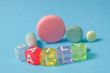 Word DAILY  from the letters of cubes and medical pills. Colored pills and capsule on blue background. Pharmacy Theme,