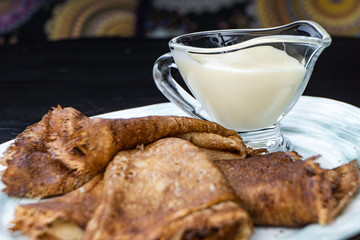 Stack of pancakes on a plate with sour cream. Traditional for the Russian pancake week. Dark background