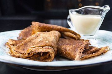Stack of pancakes on a plate with sour cream. Traditional for the Russian pancake week. Dark background