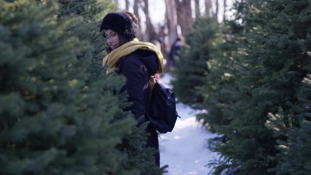 Beautiful woman in winter walks through rows of christmas trees at christmas tree farm
