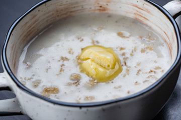 Morning Breakfast, oatmeal on milk with butter in white plate on dark background