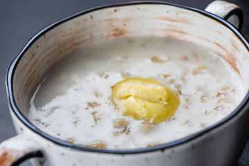 Morning Breakfast, oatmeal on milk with butter in white plate on dark background