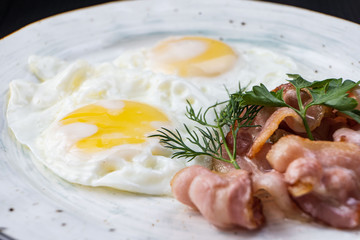Scrambled eggs and bacon in a white plate on a dark background close-up. Omelet