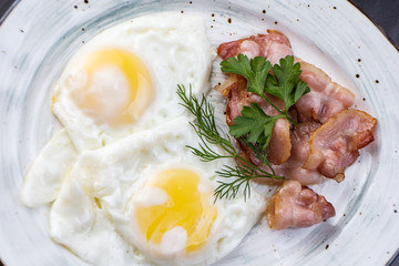 Scrambled eggs and bacon in a white plate on a dark background close-up. Omelet