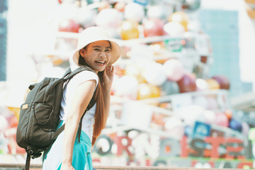 Asian girl looking for people to ask direction to travel and shopping in the department store near middle of the big city. She is excited and has a bright smile. Soft focus and blur. Backpack concept.