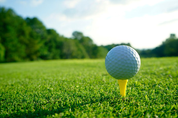 Golf ball on tee in beautiful golf course at sunset background.