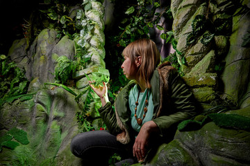 Naklejka na ściany i meble Girl in a green jacket with blond hair near an artificial rock with a grotto. Fabulous photo shoot in the Studio