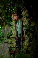 Obraz na płótnie Canvas Girl in a green jacket with blond hair near an artificial rock with a grotto. Fabulous photo shoot in the Studio