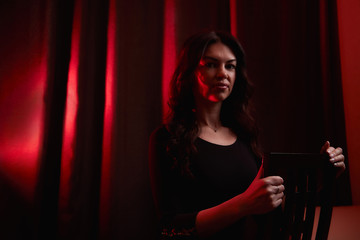 Mysterious portrait of a girl in a black dress in dark room and red light background