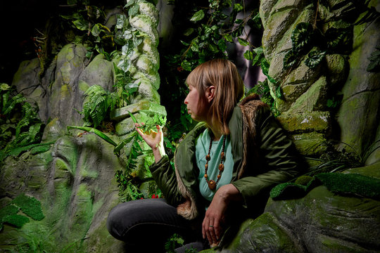 Girl in a green jacket with blond hair near an artificial rock with a grotto. Fabulous photo shoot in the Studio