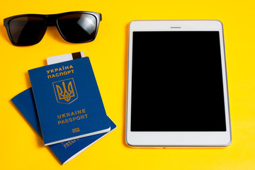 tablet, Ukrainian passport, card for payment and glasses are on a yellow background. holiday and weekend travel concept in warm and sunny countries
