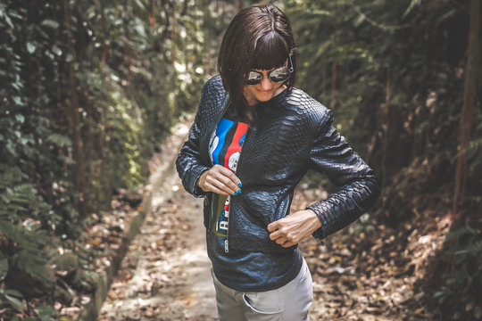Sexy young woman in luxury snakeskin python black jacket posing outdoors in the park. Bali island, Asia.
