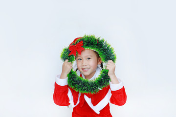 Happy little child girl in Santa costume with holding Christmas round wreath on her face on white background. Merry Christmas and Happy New Year Concept.