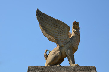 The stone griffin sits on a pedestal against the blue sky in the sunlight. Bottom view.