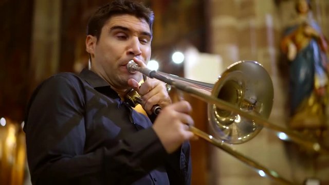 musician is playing trumpet in catholic church, he is exhaling air into tube, pressing buttons