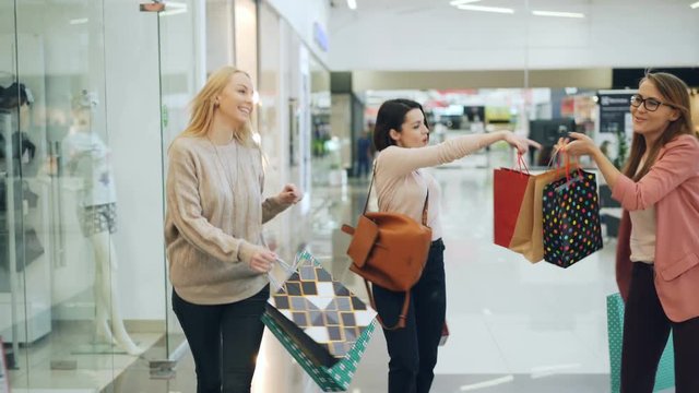 Group of happy girls is having fun in shopping center walking with paper bags, laughing and dancing pointing at goods in shop windows. Youth and shopaholics concept.