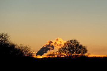 Fototapeta premium Sun setting over smoke from factory - orange look