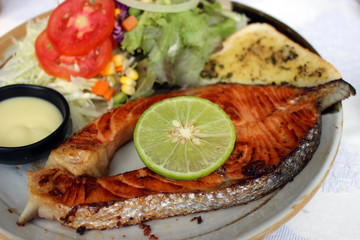 Meal of grilled salmon steak served with salad, slice of lime and sauce dip.
