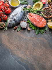 Raw dorado fish and salmon steak with spices and vegetables on the graphite board.
