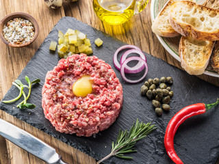 Steak tartare served with raw quail egg yolk, capers and bread. Top view.