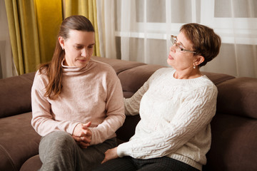 senior mother consoles, comforting sad adult grown daughter sitting at sofa at home. support in two...