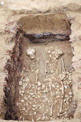Archaeological excavations. Human remains (bones, two skeletons and skulls) in the ground, with little found artefacts in the tomb. Real digger process. Outdoors, copy space, close up.