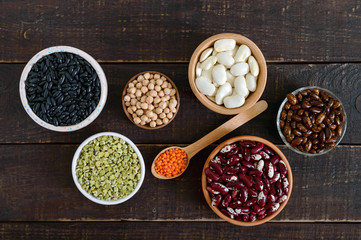 Healthy food, dieting, nutrition concept, vegan protein source. Assortment of colorful raw legumes: red lentils, green peas, beans, chickpeas in bowls, on a wooden table. Top view, flat lay background