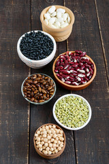 Healthy food, dieting, nutrition concept, vegan protein source. Assortment of colorful raw legumes: green peas, beans, chickpeas in bowls, on a wooden table.