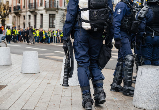 Rear view of police officers securing the zone in front of the Yellow vests movement protesters on Quai des Bateliers street detail on their guns, rifles, baton, gas tear guns, 
