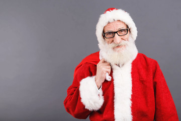 Santa Claus with a white beard wearing Santa outfit standing with the bag on the gray background, New Year, Christmas, holidays, souvenirs, gifts, shopping, discounts, shops