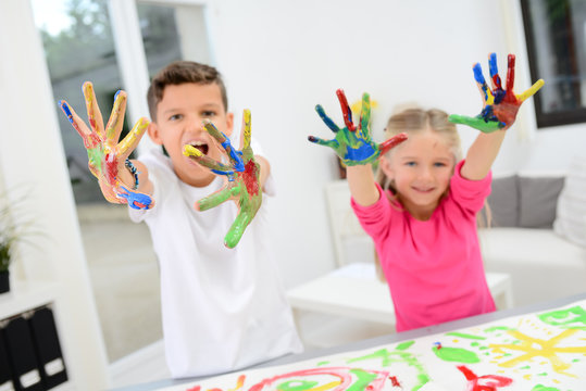 two beautiful young kids boy and girl hand painting on a white paper with color paint