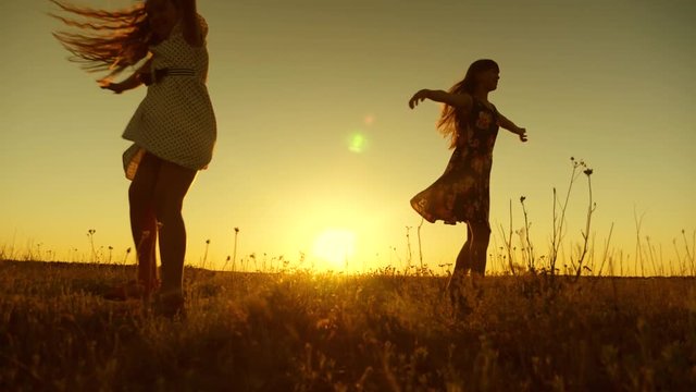 happy girls dancing in rays of beautiful sunset in park. Teenage girls with long hair whirl in flight under rays of golden sunset. Slow motion.