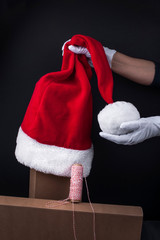 Santa Claus hat in his hands. Christmas present and santa. Black background and minimalism on a postcard. Free space for text.