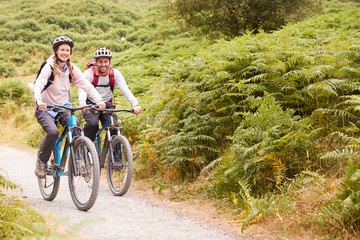 Young adult couple riding mountain bikes in the countryside, full length