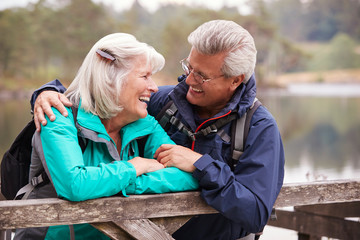 Happy senior couple leaning on a wooden fence smiling to each other, close up, Lake District, UK